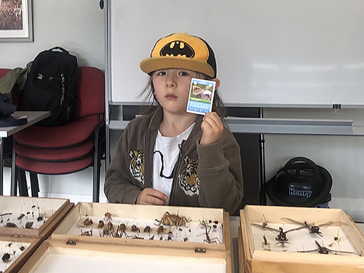 Tora with his mum at the City Nature challenge at the Leonard Cockayne Centre, Otari-Wilton’s Bush looking at a Te Papa education display and showing me his insect cards. Photo by Julia Kasper A child in a cap is holding up