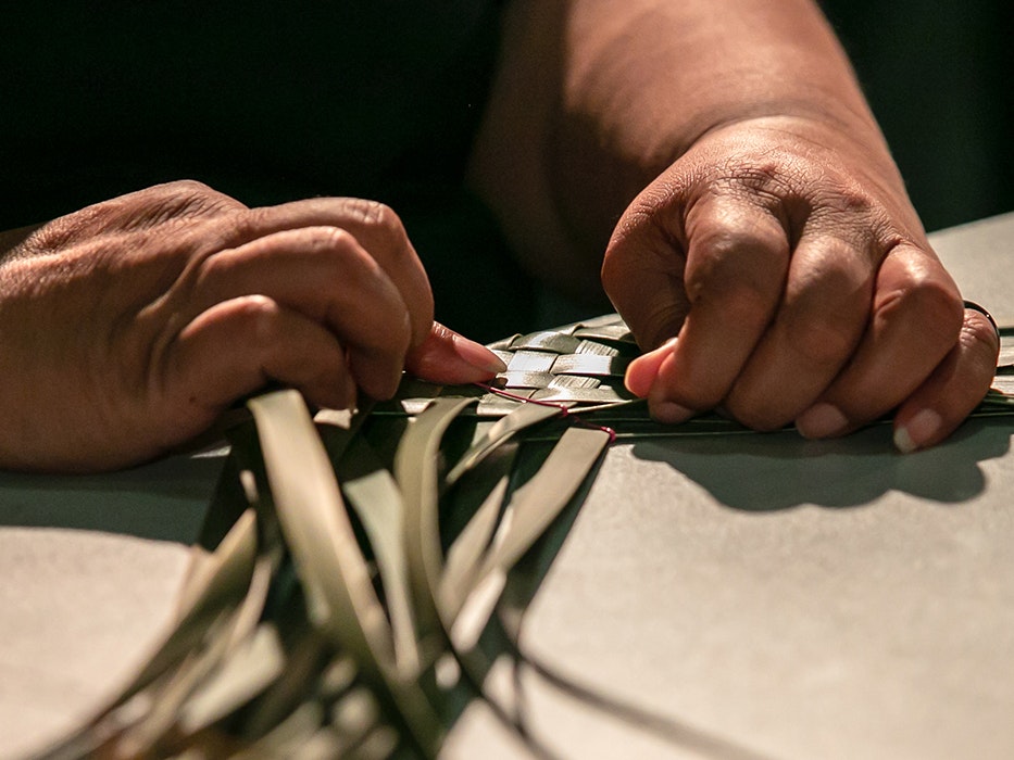 Power to the Puoro, 2021. Photo by Jo Moore. Te Papa (181511)  Two hands weaving green flax on a table.