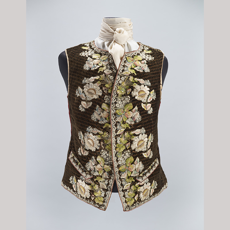 A brown tweed waistcoat on an armless mannequin with embroidered flowers on the front panels.