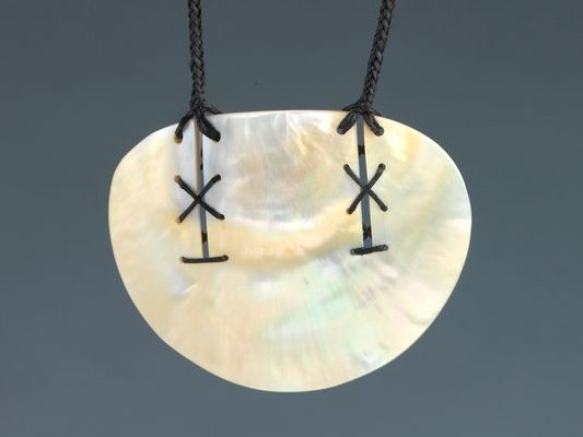 Pendant made by Sofia Tekela-Smith; around 2000; Auckland, mother of pearl, thread. Purchased 2001 with New Zealand Lottery Grants Board funds Te Papa (FE011590) A shell pendant with markings on it and cord attached.