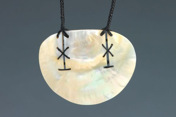 A shell pendant with markings on it and cord attached.