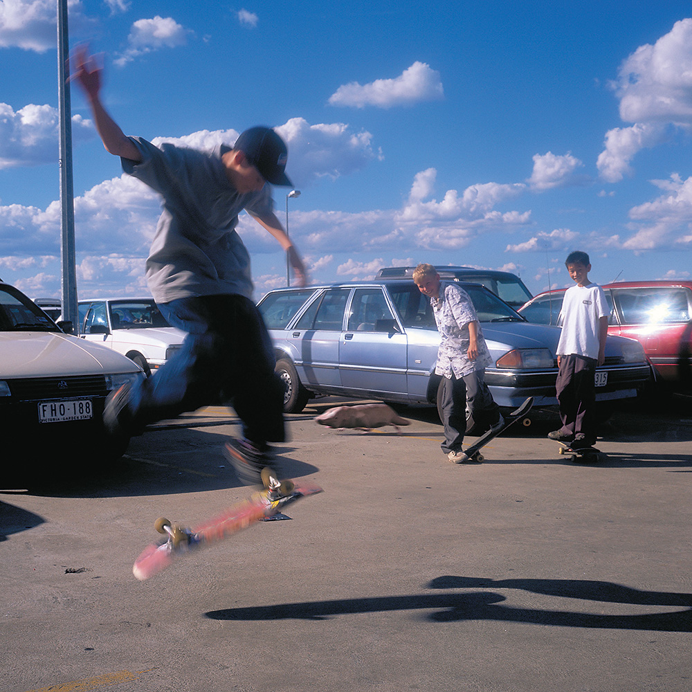 A photo of three kids skateboarding in carpark.