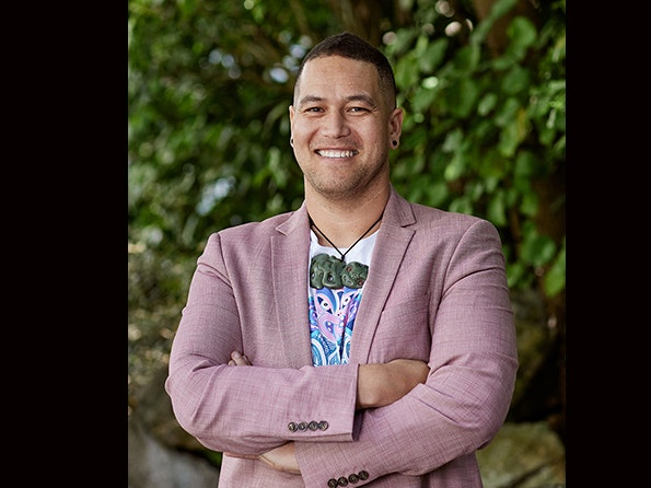 Isaac Te Awa. Photo by Yoan Jolly. Te Papa (237514) A man in a pink jacket and a t-shirt is smiling at the camera.