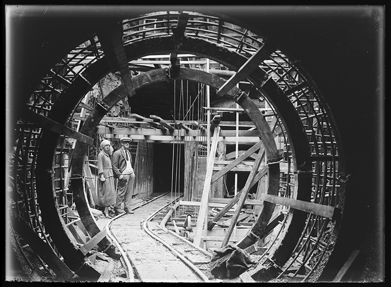 A black and white photo of a man and a woman standing next to a railway track with a tunnel shape framing them.