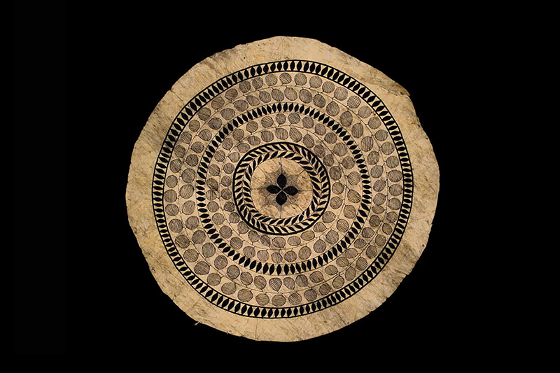 A round tapa cloth with painted patterns on it.