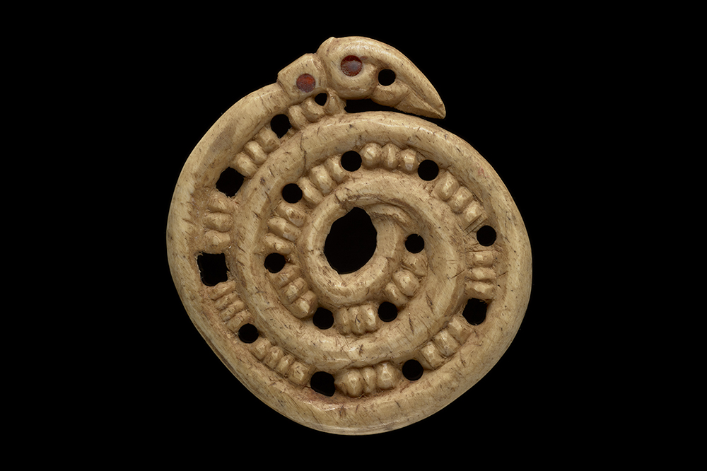 A spiral carving with holes every four notches. There is a ahead at the end of the spiral with red beads for eyes.