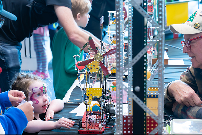 Child stares intently at a model windmill created using Meccano pieces