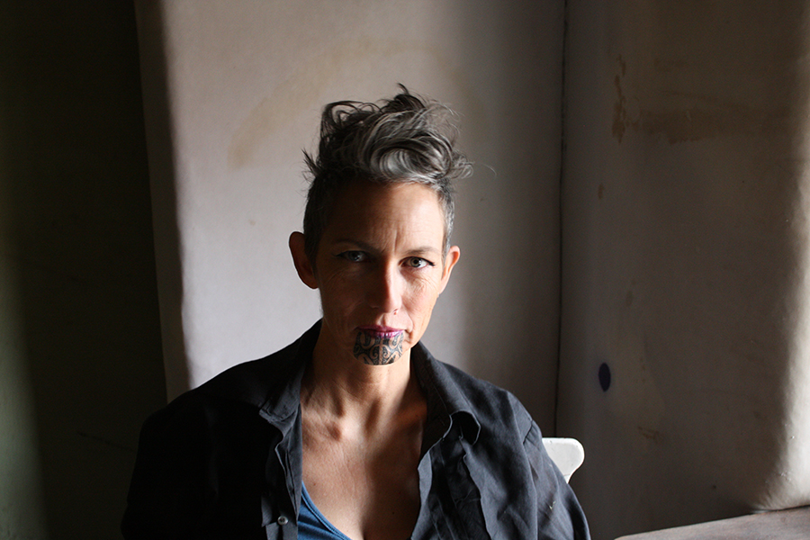 A shadowy head and shoulders of a woman with spiky hair staring intently at the camera.