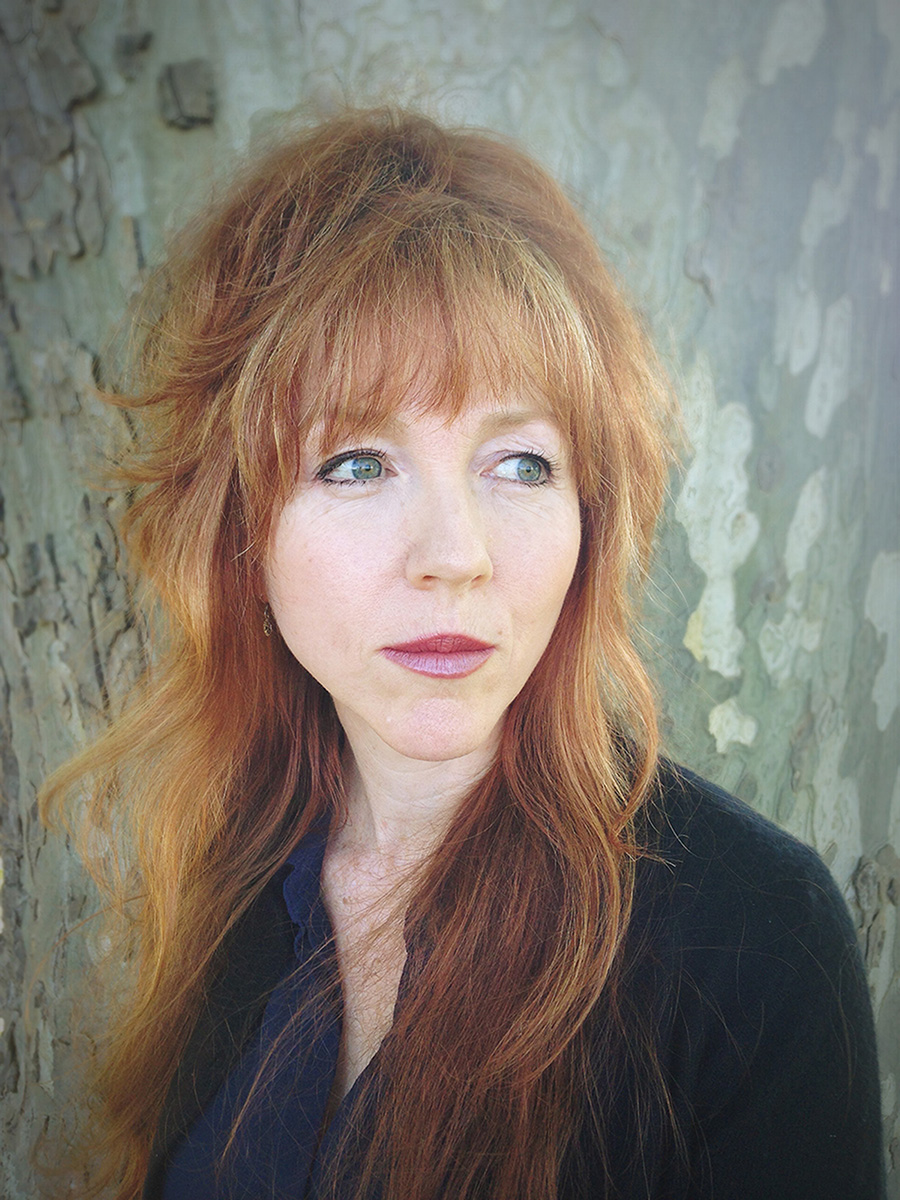 Head and shoulders photo of a woman with long red-blonde hair. She is looking off into the distance.