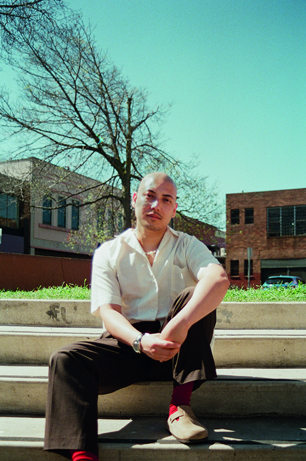 A man is sitting outside on concrete steps looking at the camera.