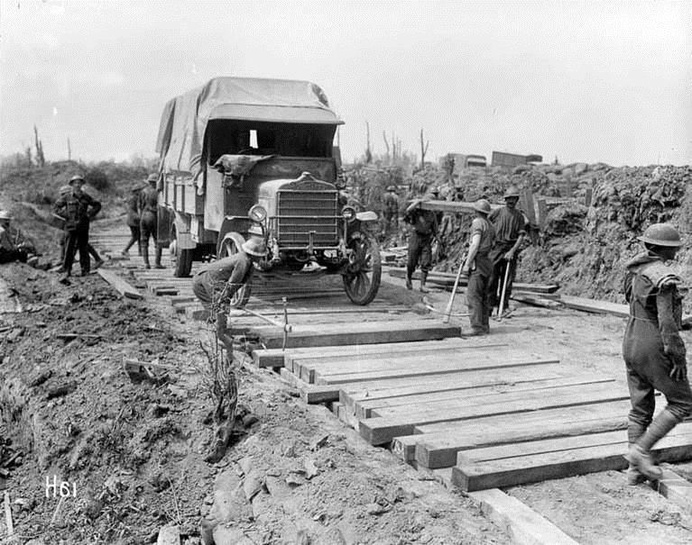 A black and white photo of men working in a war zone building a wooden road for a truck to pass.