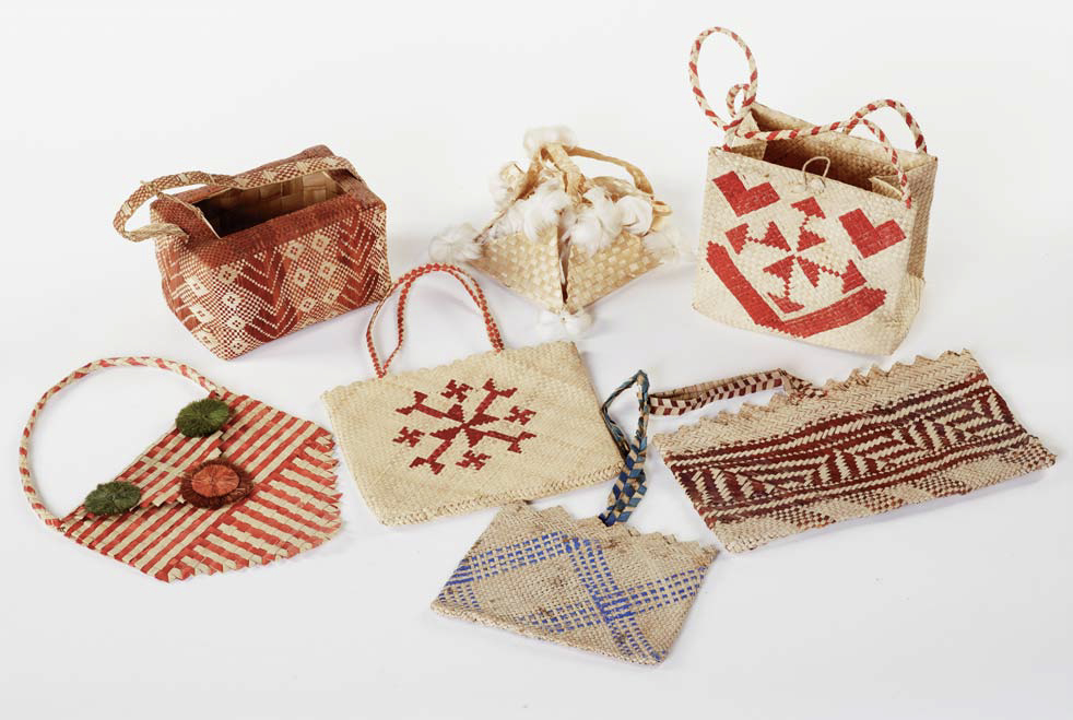 Seven woven items made of light brown, red, and blue pandanus leaves.