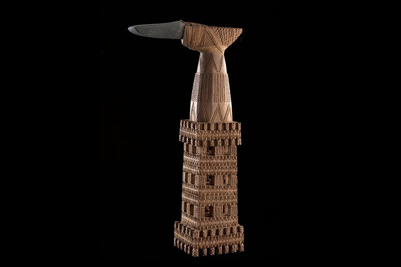 A stone adze with an intricately carved wooden handle bound to it with sennit.