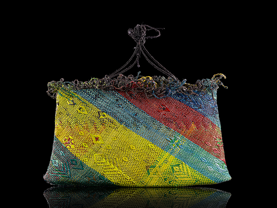 A woven bag or kete with two handles. There iare briggly coloured patterns woven into the sides.