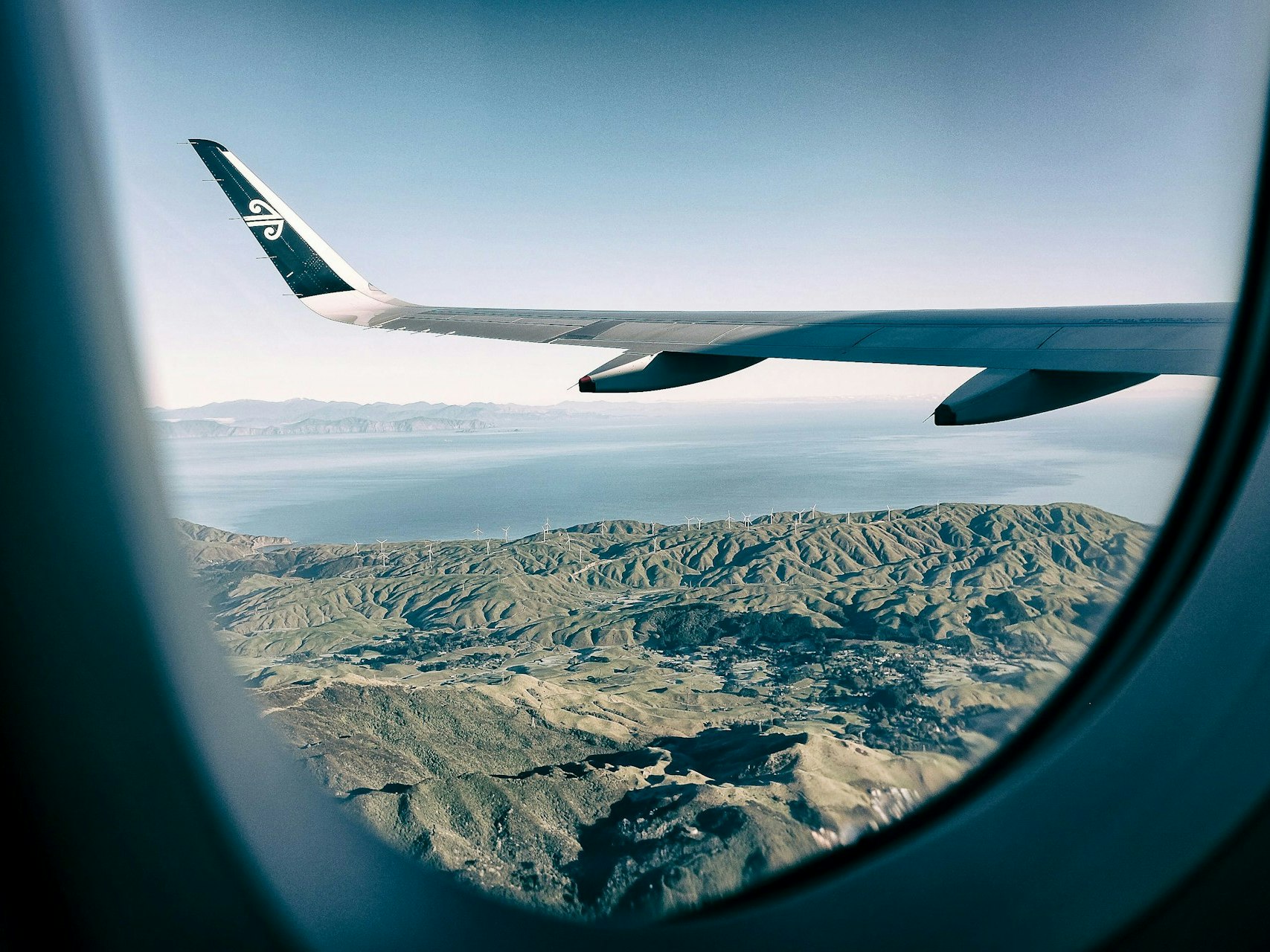 Photo by James Coleman. Unsplash A view from a plane window, looking out over the plane wing and the land below.