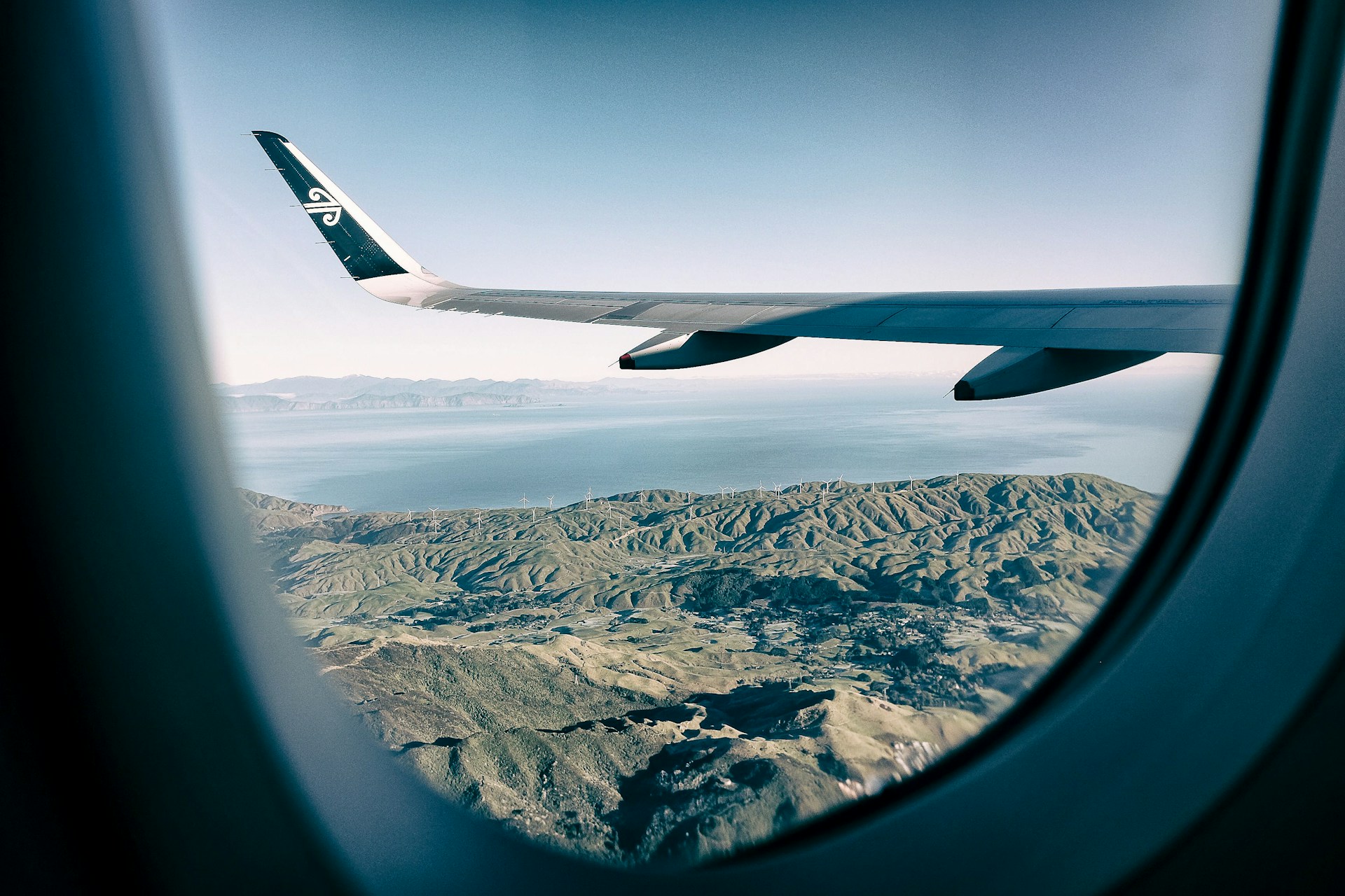 A view from a plane window, looking out over the plane wing and the land below.