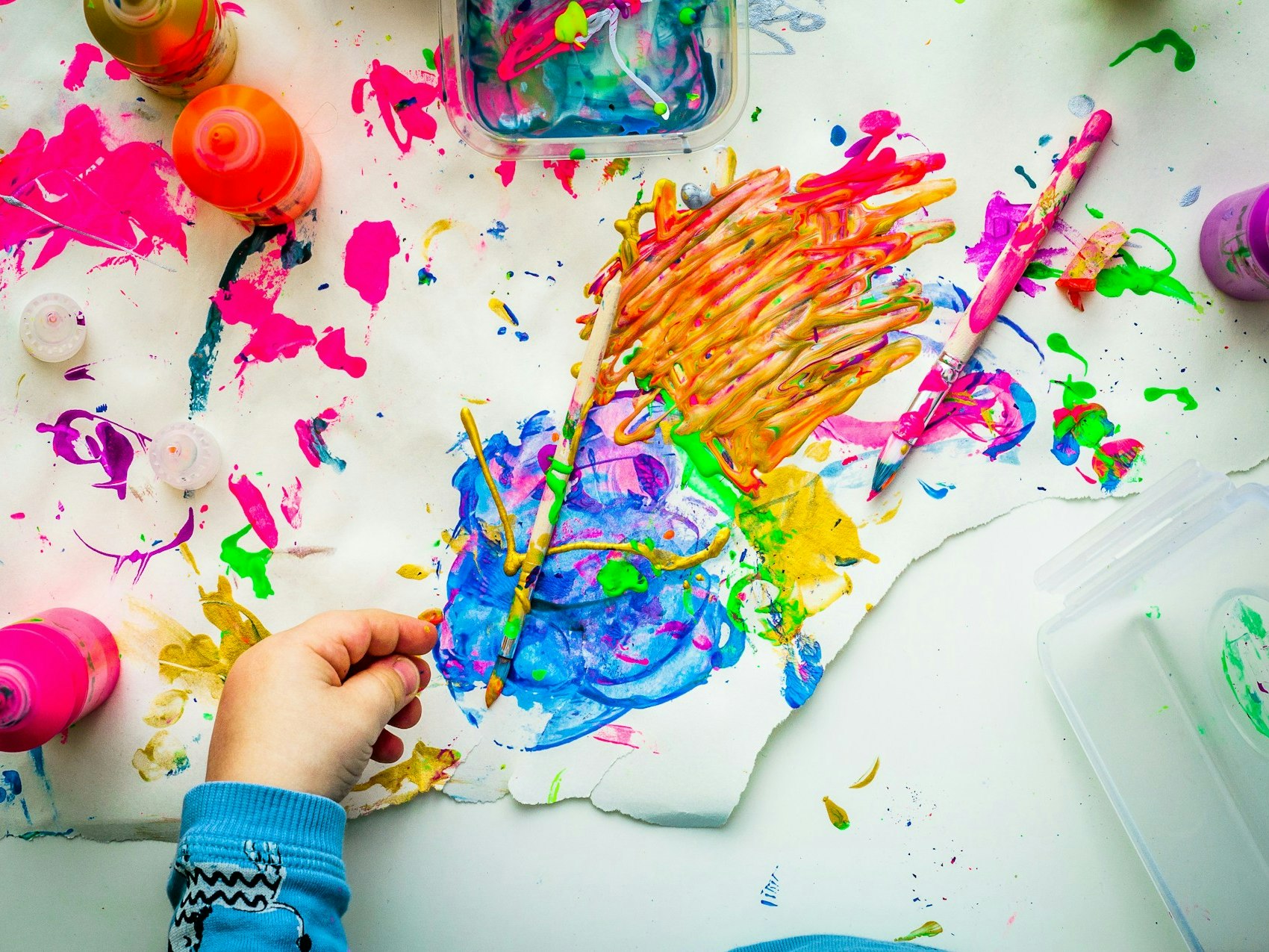 Photo by Dragos Gontariu on Unsplash A photograph of a desk with a lot of paint colours everyone and one hand resting on the desk.