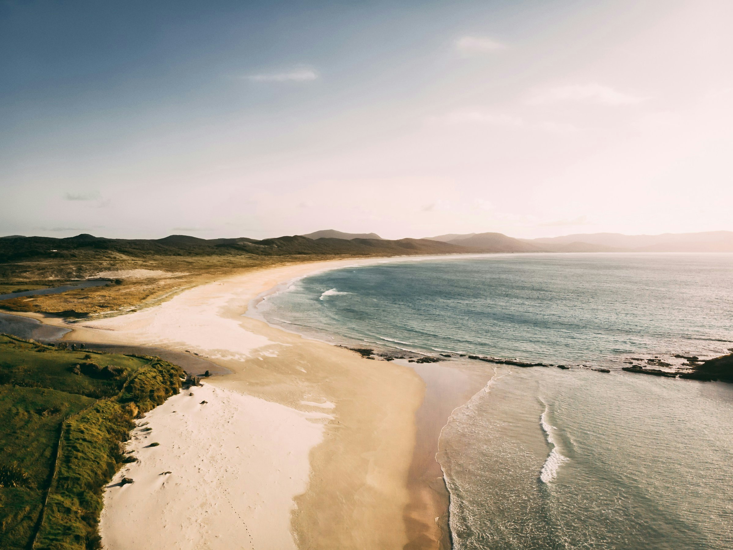 Photo by Andre Bernhardt. Unsplash. A photo of a long sandy beach with the sea lapping at the shore.