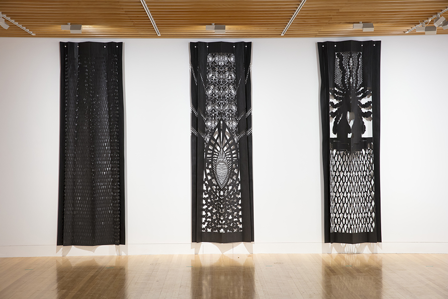 A photo of three long black and white panels hanging in an art space.