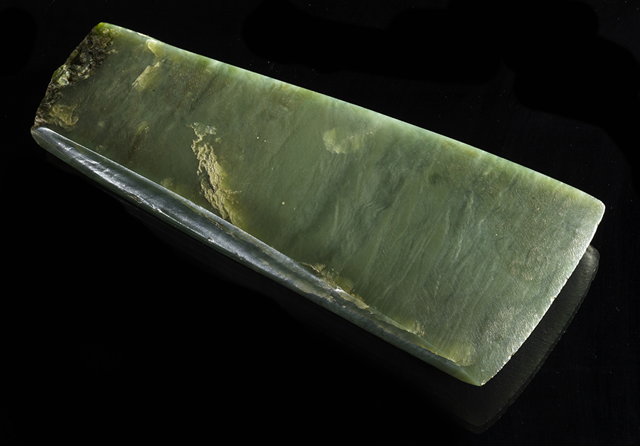 A pounamu or greenstone adze on a black background.