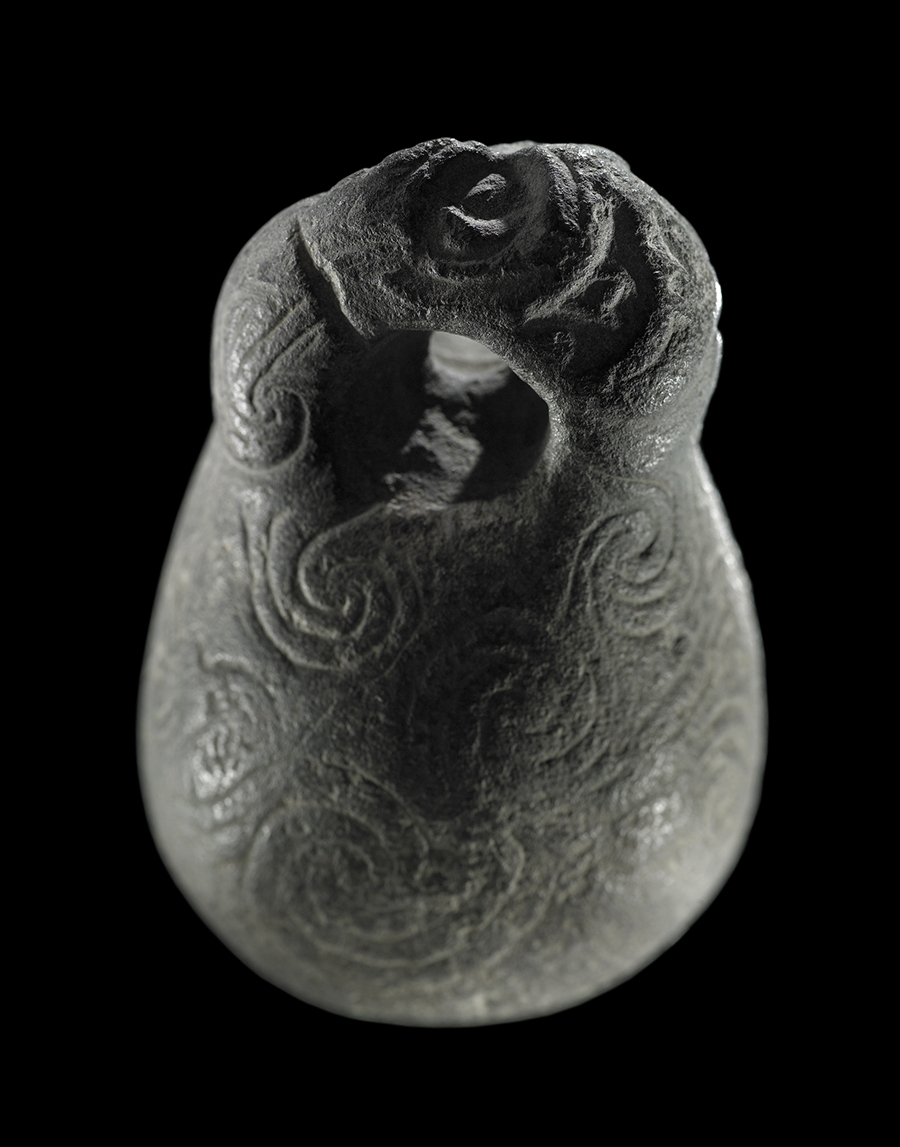 A bulbous stone with a hole carved in the top and coiled shapes carved on the sides.