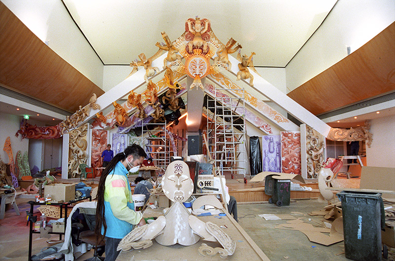 A man is sitting in the foreground working on a sculpture for a stage in the background.