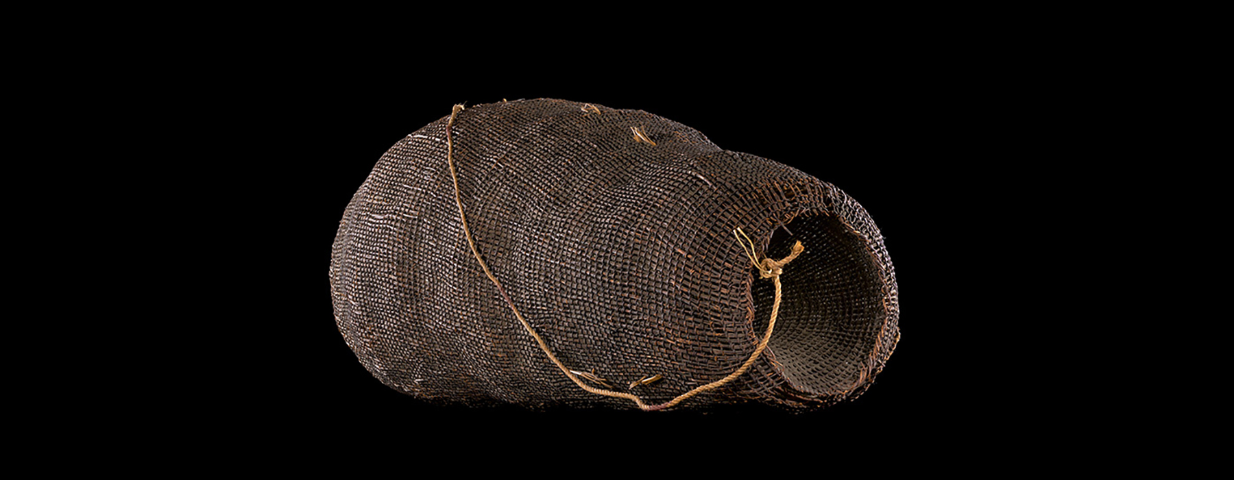 A woven basket with a plaited handle sitting in a black background.