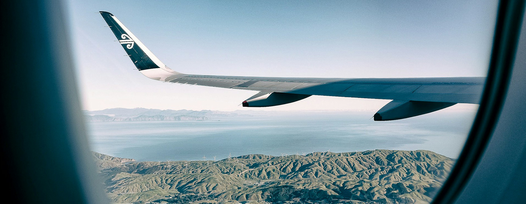 A view from a plane window, looking out over the plane wing and the land below.