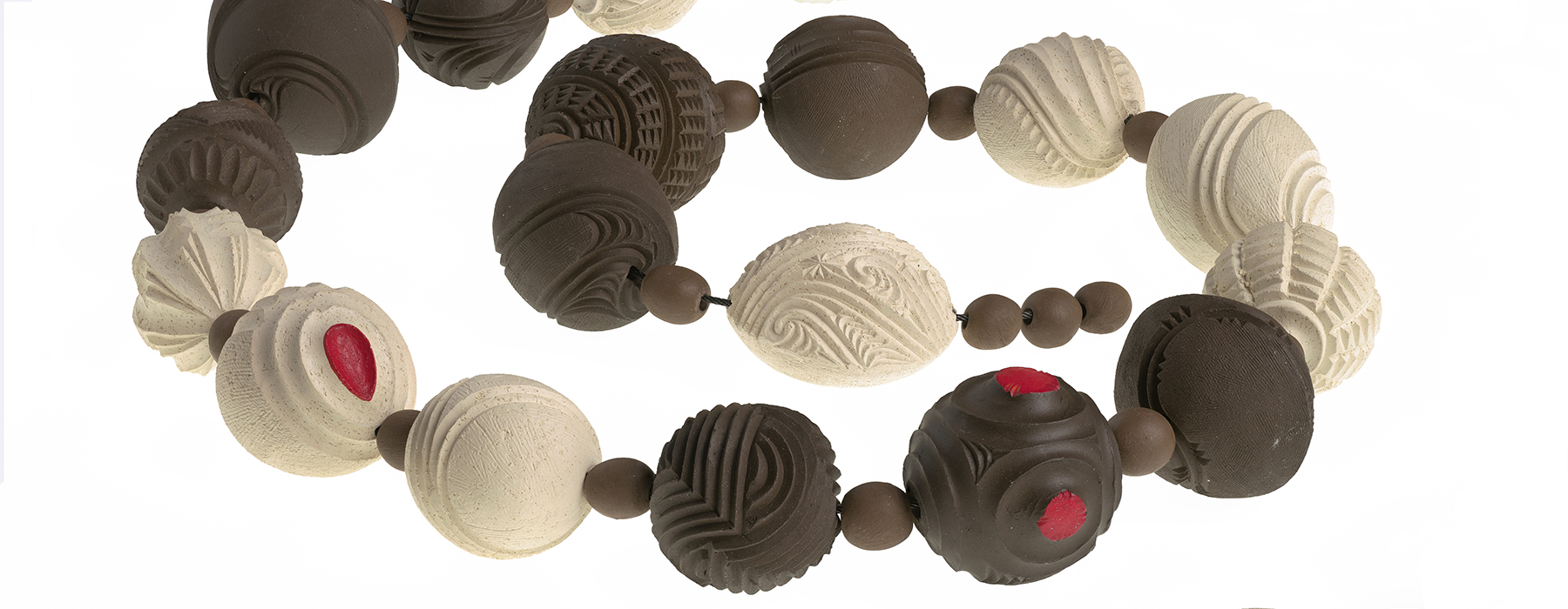 A string of clay beads in a coil. Some of the largerr beads are dark brown clay, some are white, and somc of them have red dots on them.