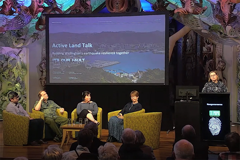 Four people on a stage with a large screen behind them.