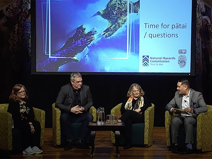 Active Land talk panel. Photo by Te Papa Two men and two women are sitting on a stage talking to an unseen audience. There is a large projection screen behind them.
