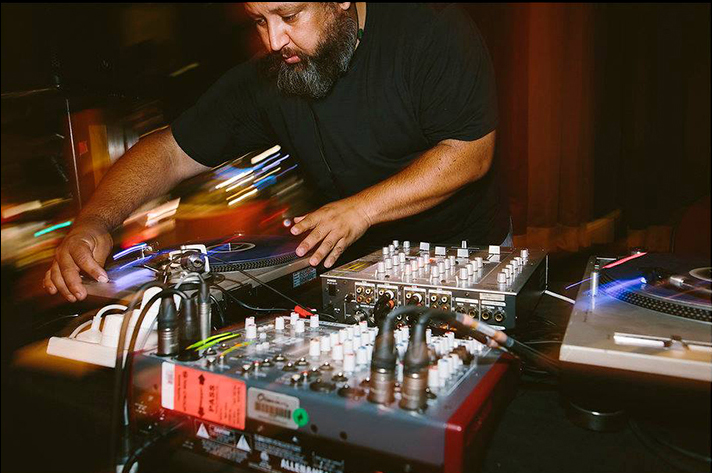 A man with a beard is working a music mixing desk.