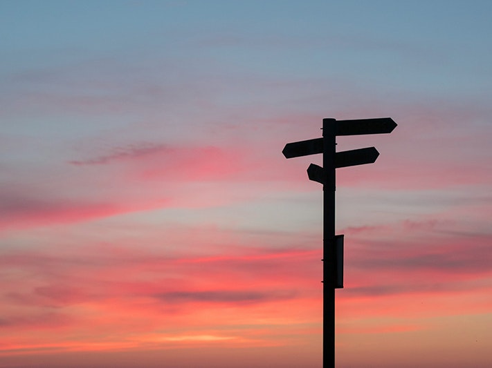 Photo by Javier Allegue Barros. Unsplash A roadsign with three different directions silhouetted against a sunset.