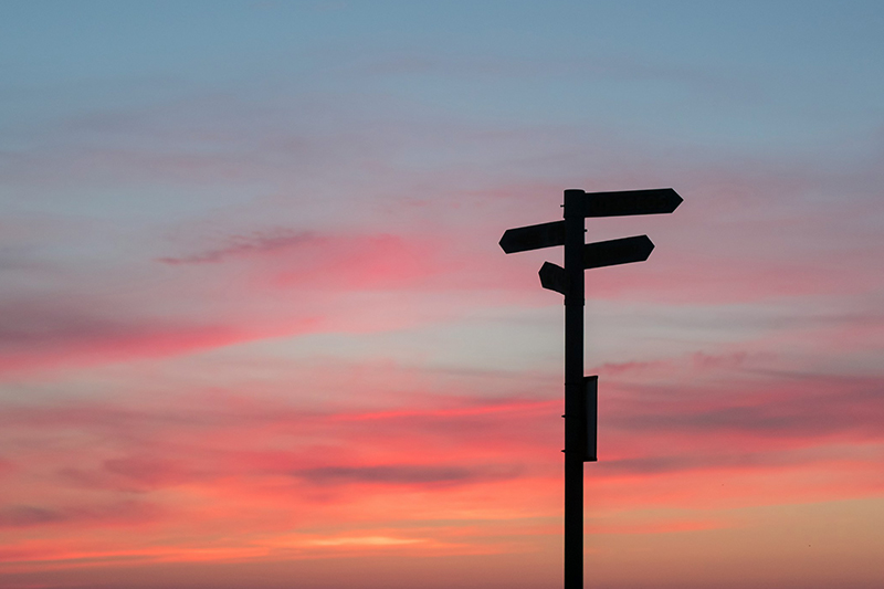 A roadsign with three different directions silhouetted against a sunset.