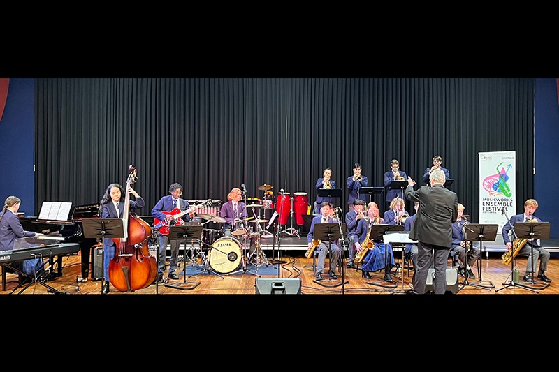 A large band of students playing instruments on a stage.