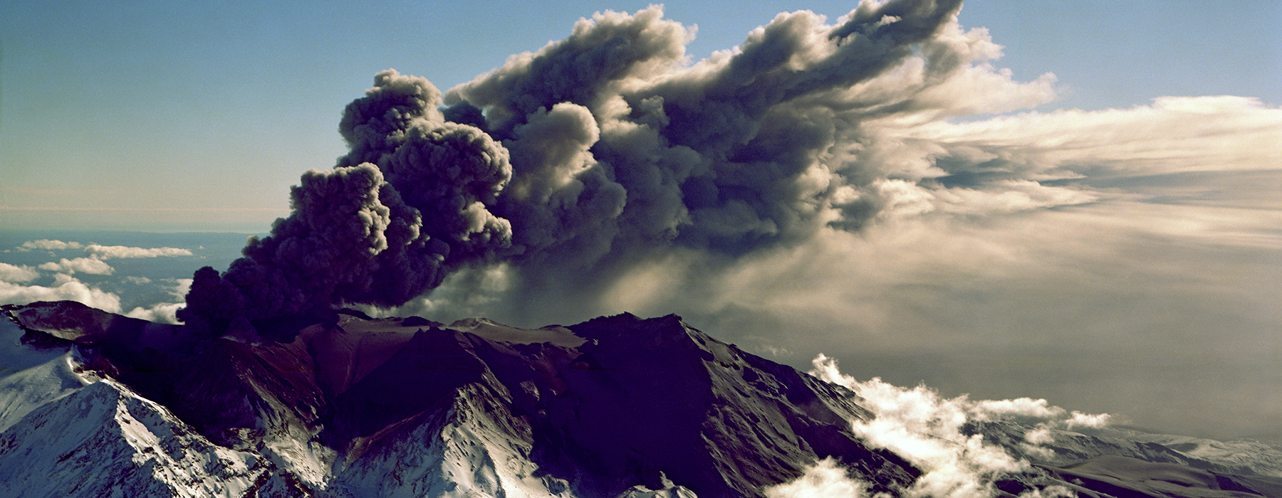 A snow-topped volcano that is spouting volcanic ash and smoke.