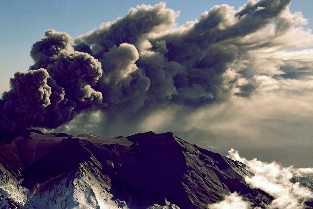 A snow-topped volcano that is spouting volcanic ash and smoke.