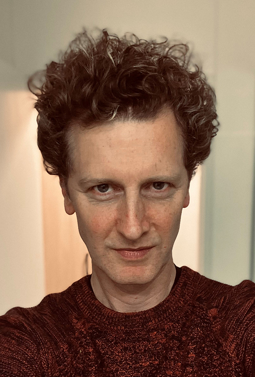 Close up of a man with wild curly hair looking intently at the camera.