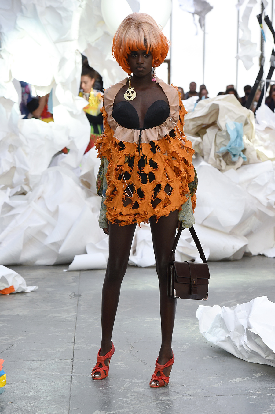 A model on a runway wearing an orange and black dress and an orange and white wig.