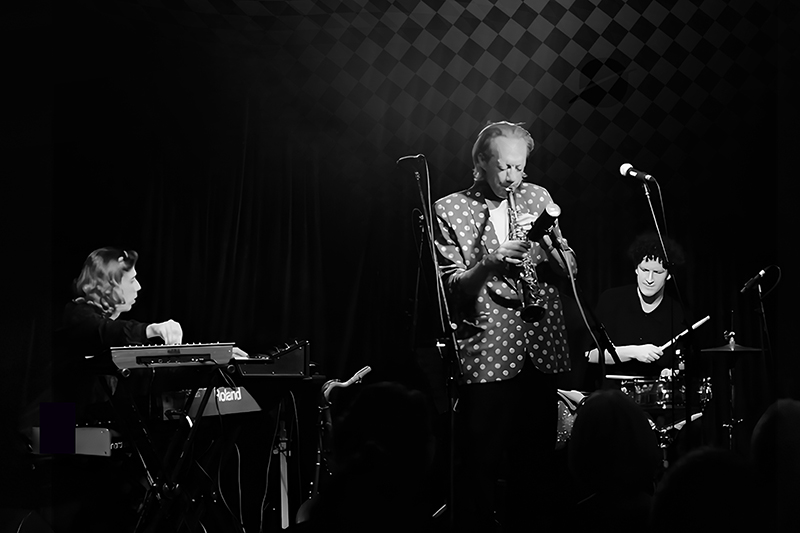 Black and white stylised photo of three musicians performing on stage.