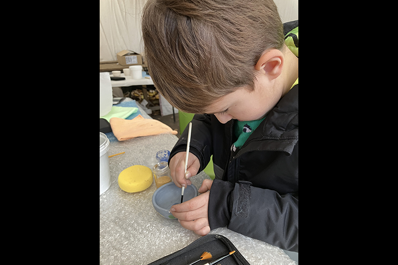 A child is carving something into a clay bowl he is holding