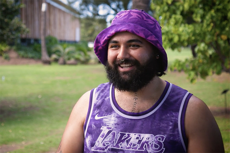 A man in a purple bucket hat and a purple singlet is talking to someone off camera.