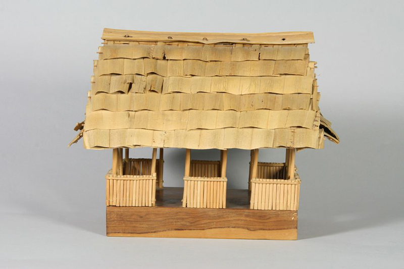 A small model house with open walls made with plant fibre, Pandanus (textile), wood, cane, plastic, nylon, and coir.