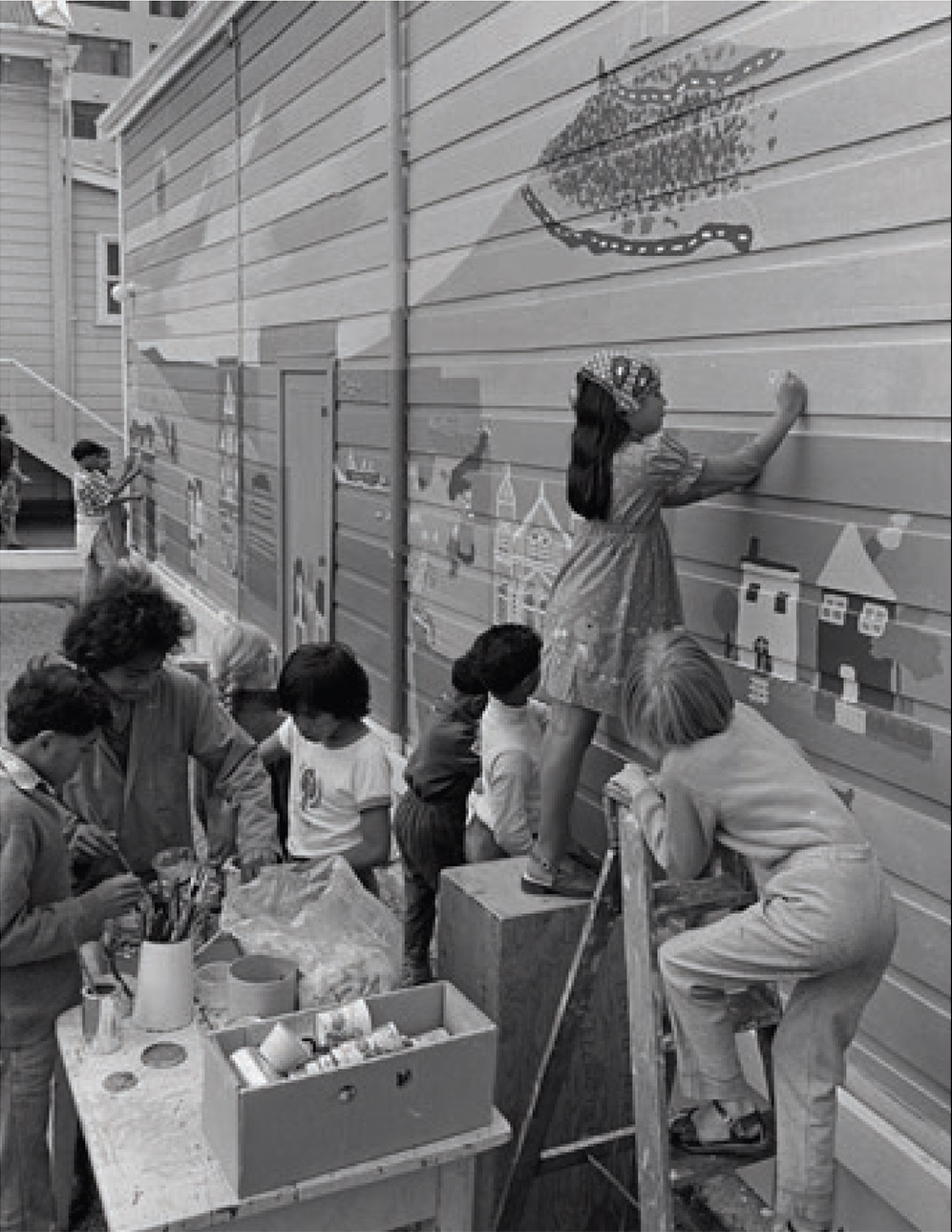 A black and white photo of children painting a mural on a wooden building