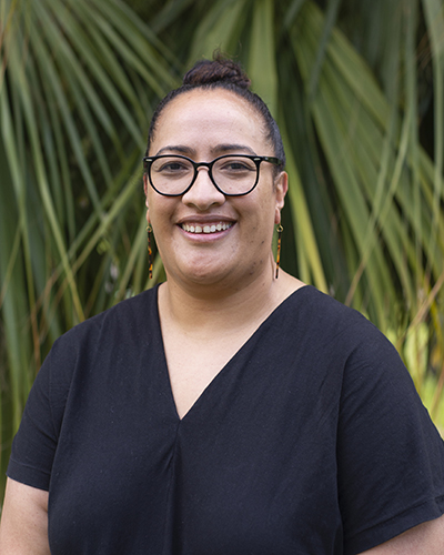 Head and shoulders photo of a woman with her hair up, wearing glasses, and standing in front of a palm tree.