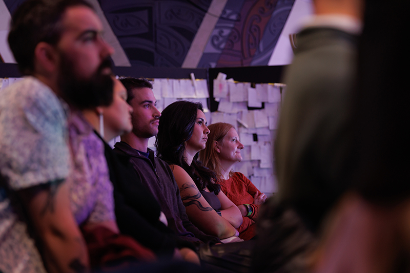 Several people sitting in a dimly lit room listening to a person off camera,