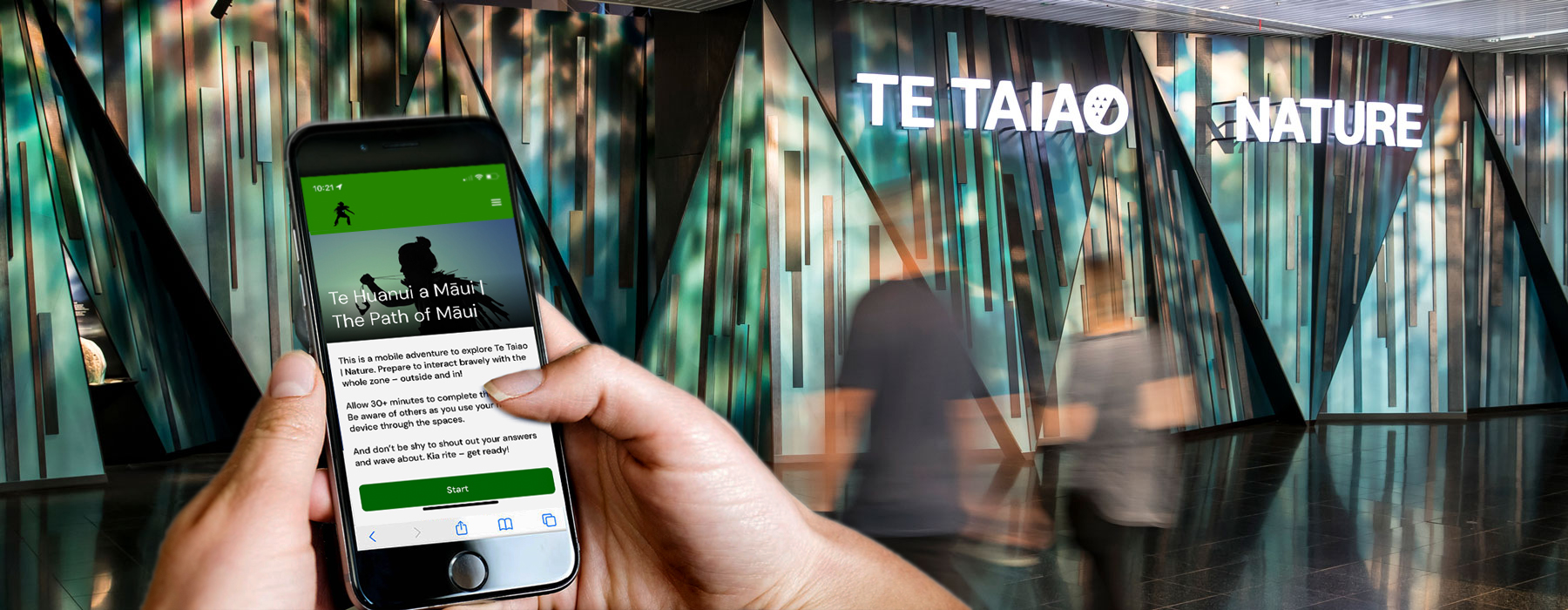 A pair of hands is holding a phone device in front of an exhibition experience in a museum