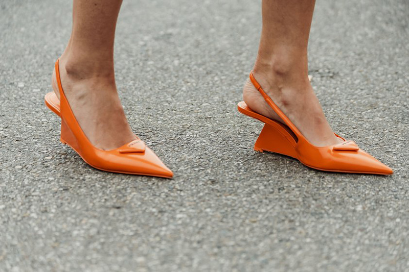 A close up of a person's feet in orang slingback shoes with strange angular heels.