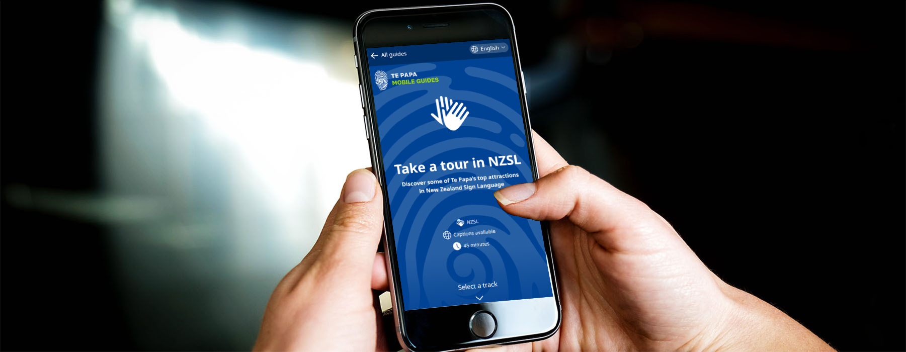 Closeup of hands holding a mobile phone which is displaying the NZSL mobile guide.