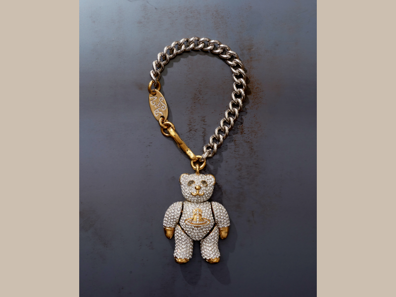 A diamond studded teddy hangs from a chunky silver chain necklace. It bears a golden Westwood symbol on its torso, with gold accents on the paws, nose and mouth. The gold clasp is engraved A&V.